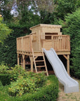 A large platform with handrail and cubby house and slide against a beautiful green hedge