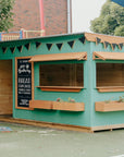 A green bakery cubby house in a school yard with chalkboard and timber accessories