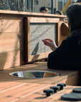 School teacher writing on wooden mud kitchen chalk board with sink, hotplates and knobs in foreground