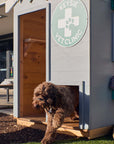 Close up of a vet themed grey and green cubby house doorway and matching doggy door with a cute dog leaping through the doggy door