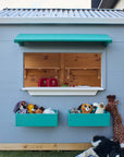 A vet themed grey and green cubby house shot from the side showing a large window in a school yard staged with soft toys