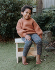 A girl sits happily on a wooden carpenter stool
