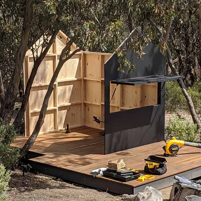A wooden Barn Style cubby house half erected showing tools lying around as if the builder is on a break.