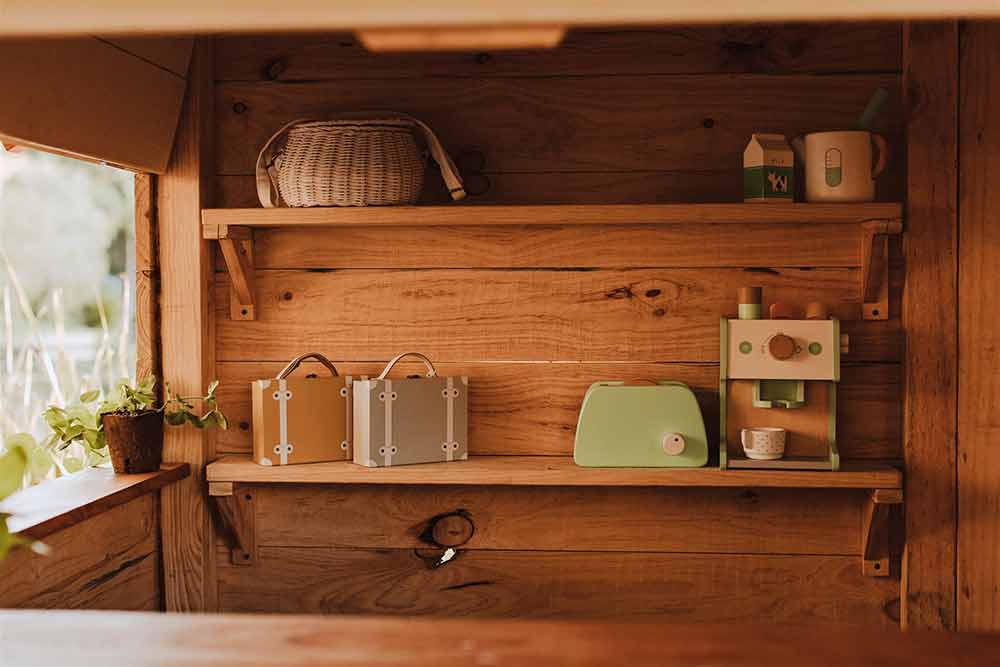 A wooden Shelf with trinkets and toys on it, inside a wooden cubby house.