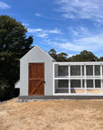 Large grey barn style chicken coop with white chicken run on a sunny day in landscape with a chicken in the foreground