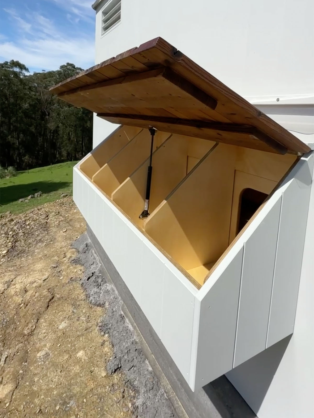Detail shot of an open plywood and thermory timber 4 way nesting box with gas strut lid on side of chicken coop