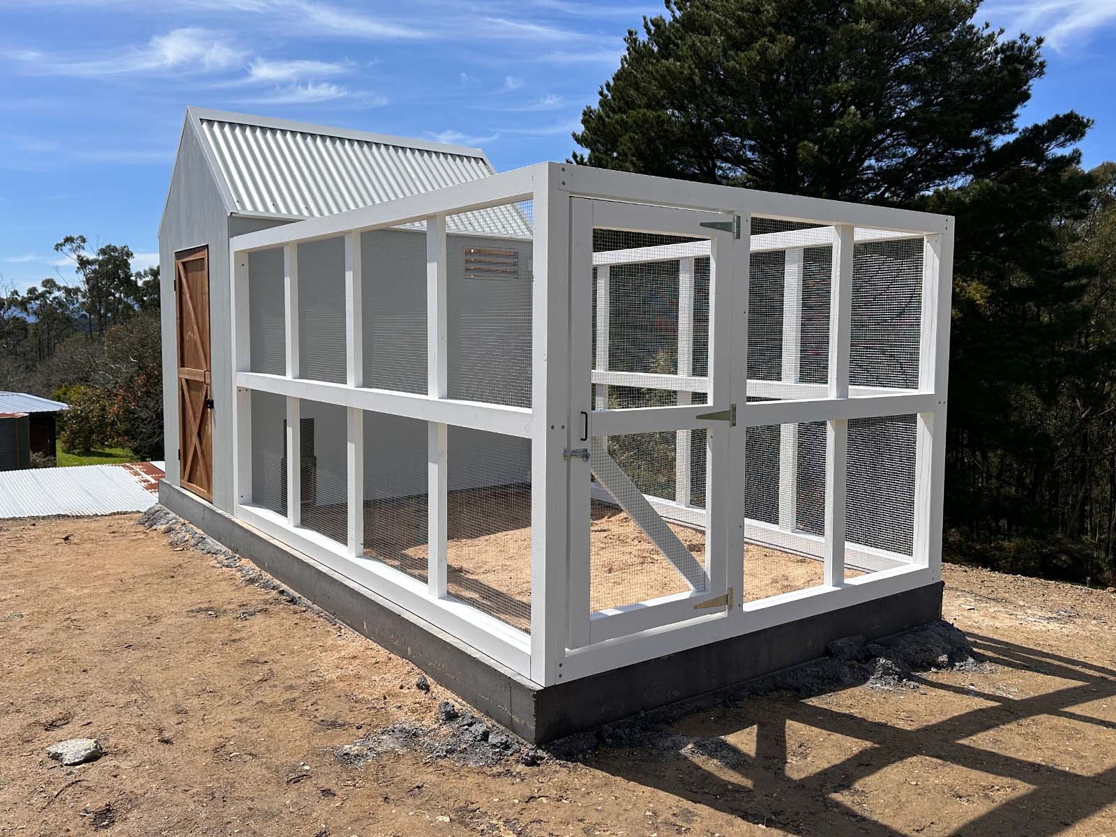 White timber chicken run and gate attached to a large barn style chicken coop on a sunny day