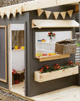 A wooden cubby house with front verandah styled with toys and painted charcoal and white