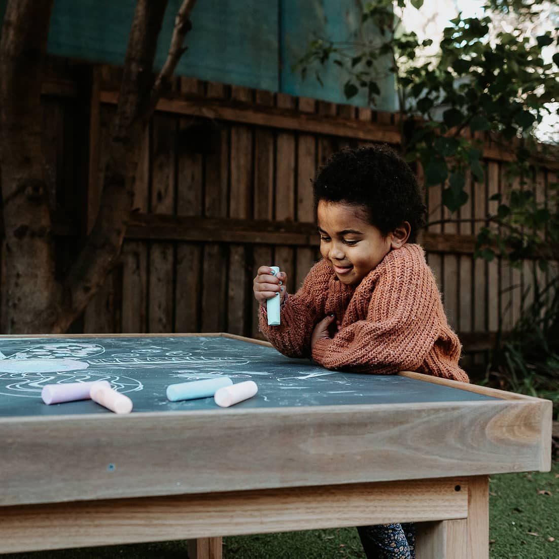 A young girl smiling and drawing on a wooden chalkboard table