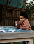 A young girl smiling and drawing on a wooden chalkboard table