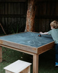 A boy drawing on a chalkboard table in an early learning centre yard