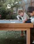 Kids gathered around drawing on an outdoor chalkboard table