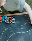 A boy plays with toy cars on a chalkboard table with drawn road map