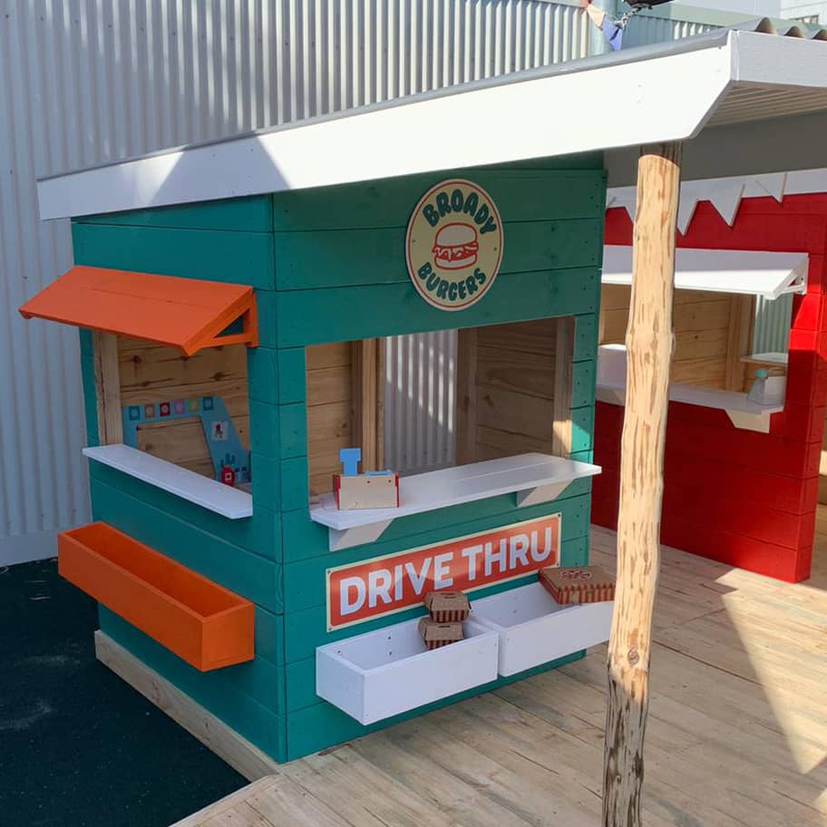 A green painted wooden burger shop cubby house in a school playground