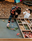 Educator and child creating a design on the chalkboard tabletop of an Exploration & Loose Parts Table in an outdoor ELC.