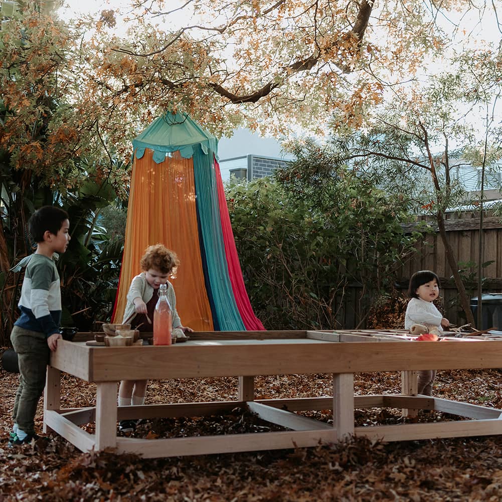 Children engaging with an Exploration & Loose Parts Table in an outdoor ELC, using the chalkboard tabletop and sensory play items.