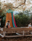 Children engaging with an Exploration & Loose Parts Table in an outdoor ELC, using the chalkboard tabletop and sensory play items.