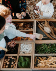 Close-up of children using an Exploration & Loose Parts Table in an ELC, with dividers holding natural materials like leaves and pebbles.