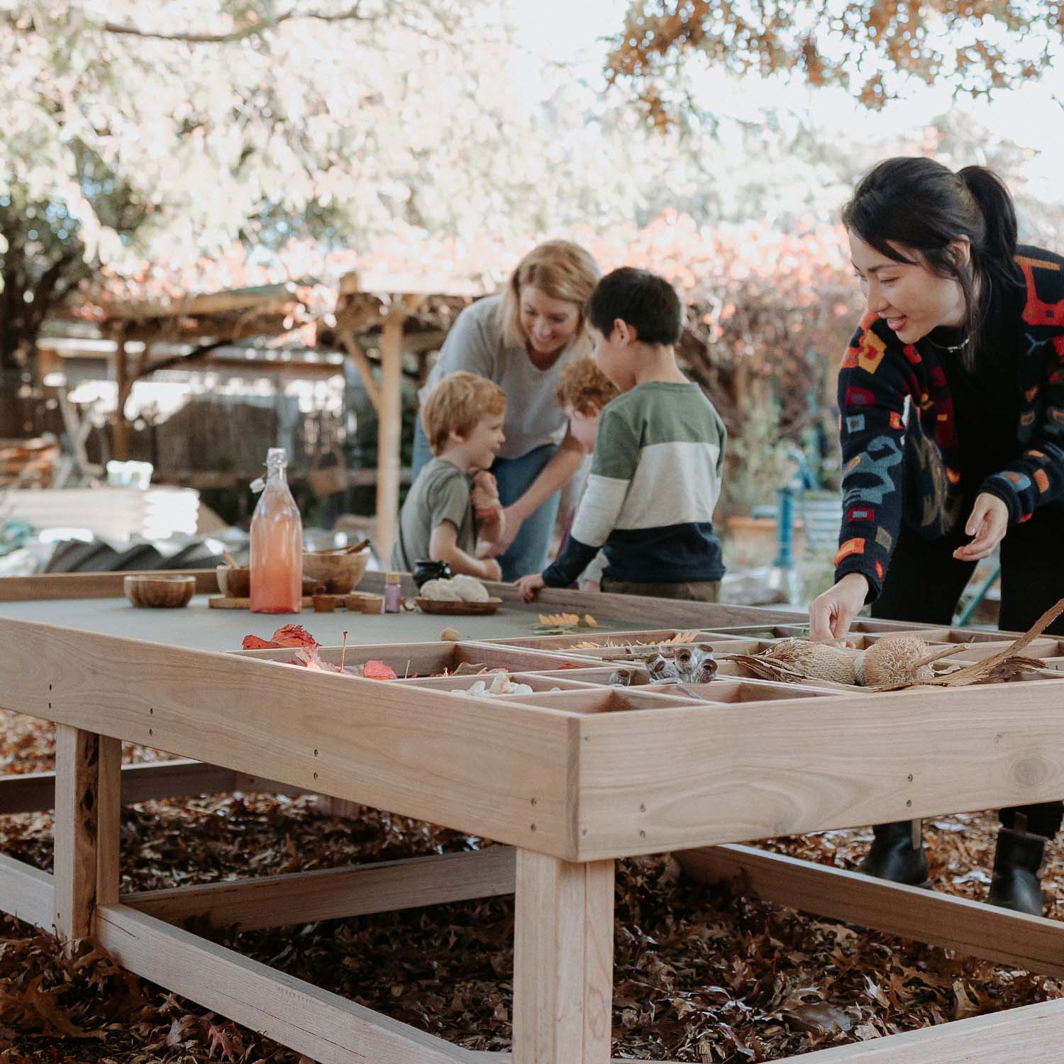 Children and educators using an Exploration & Loose Parts Table in an outdoor ELC, playing with natural materials in dividers.