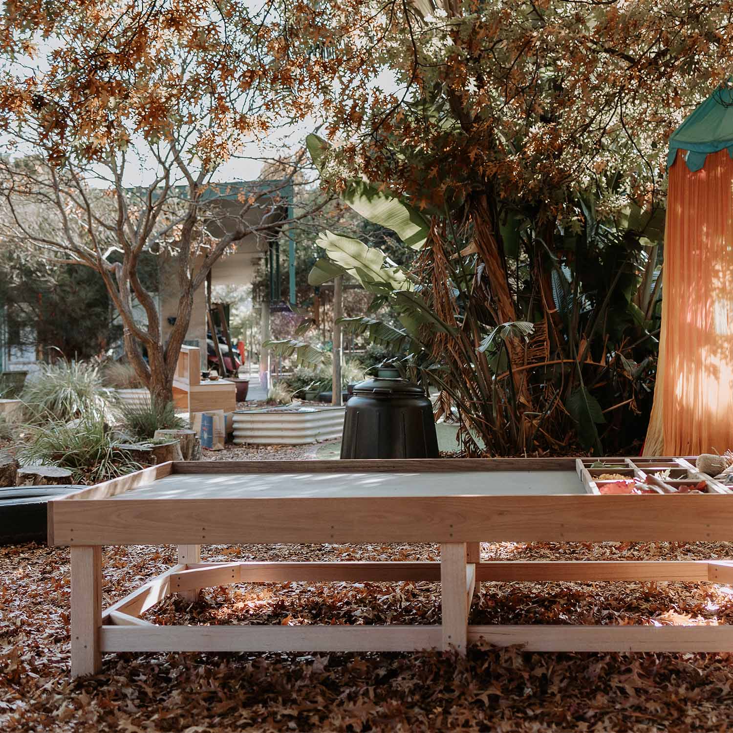 Thermory timber Exploration & Loose Parts Table in an outdoor ELC setting with natural play materials in dividers.