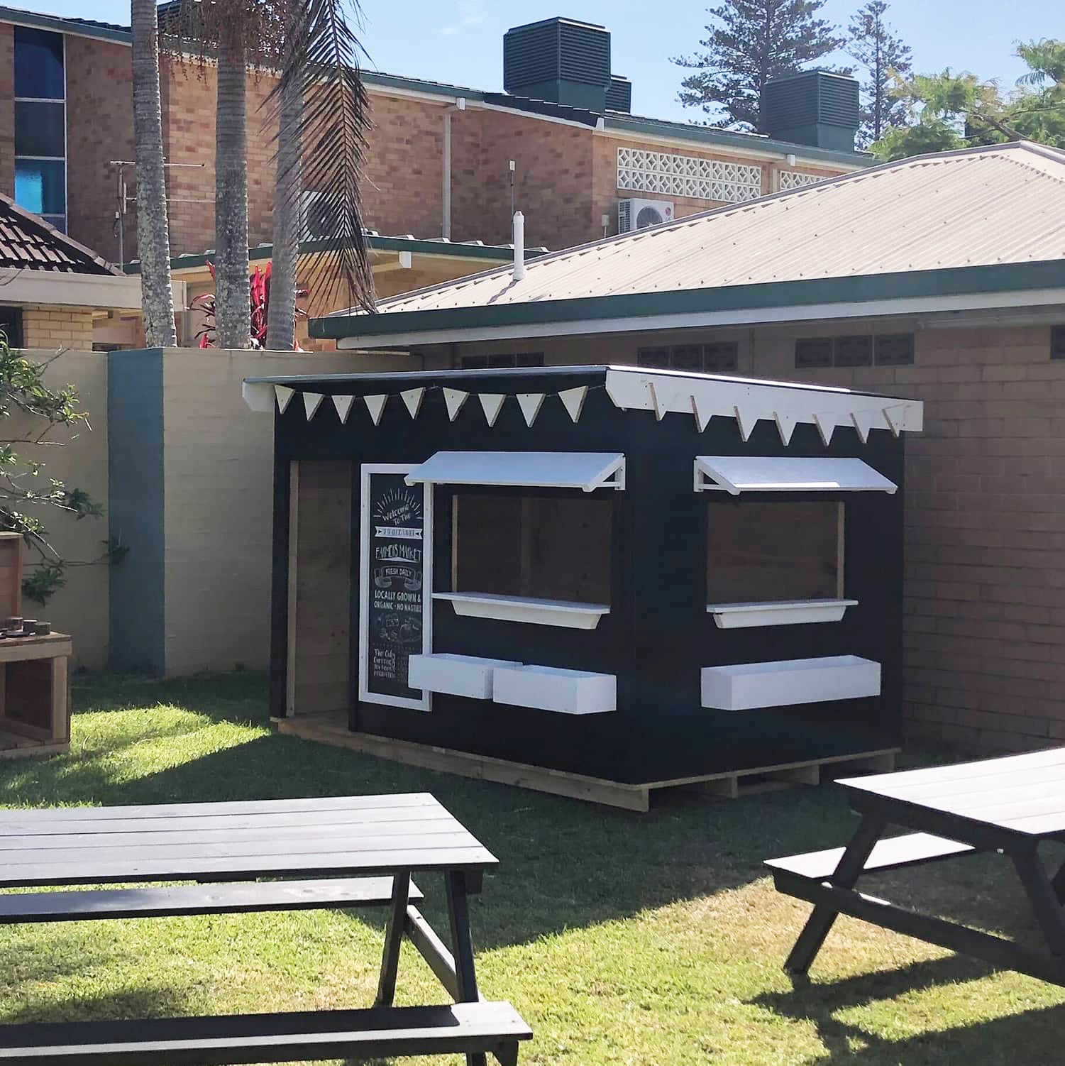 A painted farmers market themed wooden cubby house in a early learning centre play space