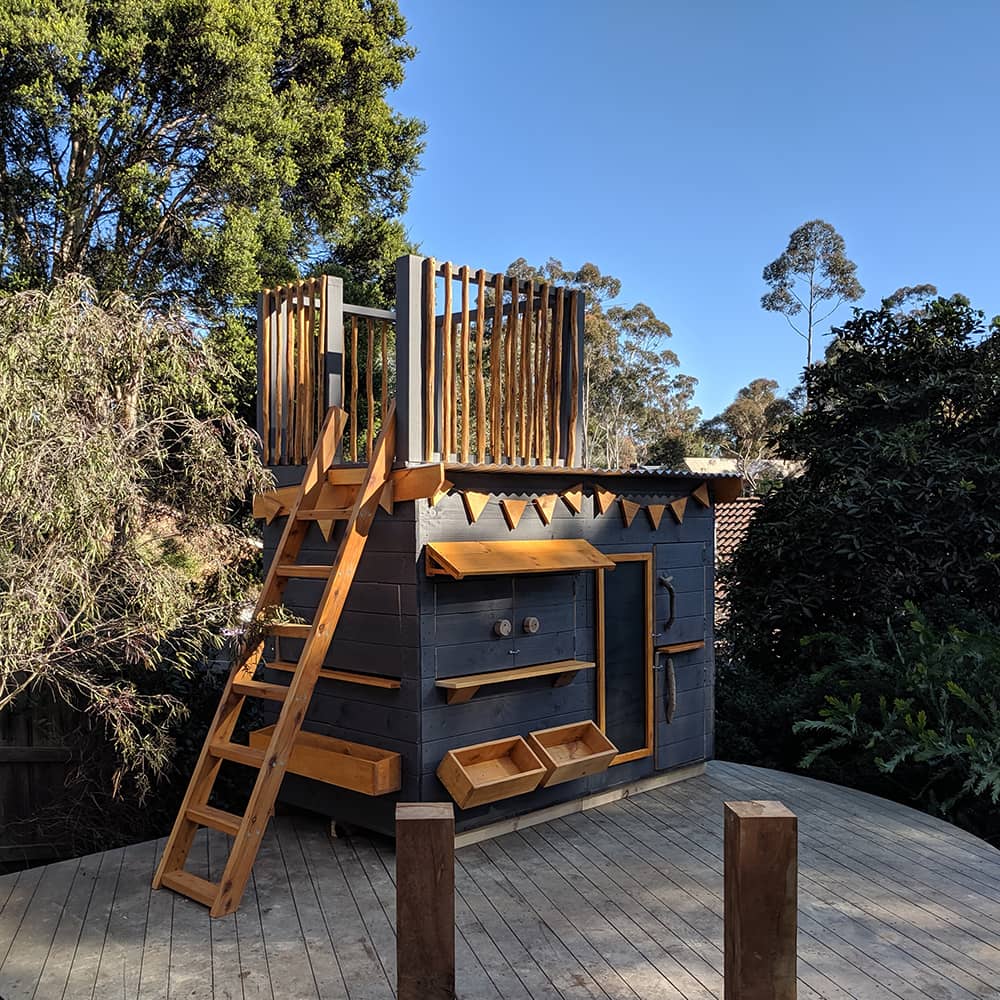 A painted wooden fort top cubby perched on a deck in a beautiful garden