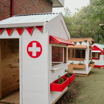 A painted wooden hospital themed cubby house with red cross sign