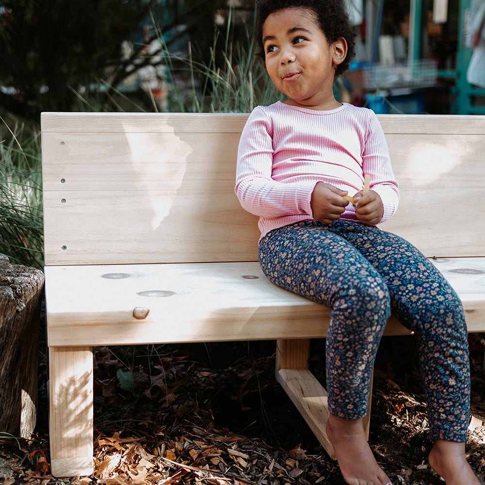 A gril rests smiling on a wooden bench seat outdoors