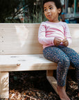 A gril rests smiling on a wooden bench seat outdoors