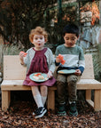 Two kids sitting on a bench seat with back enjoying a fruit snack