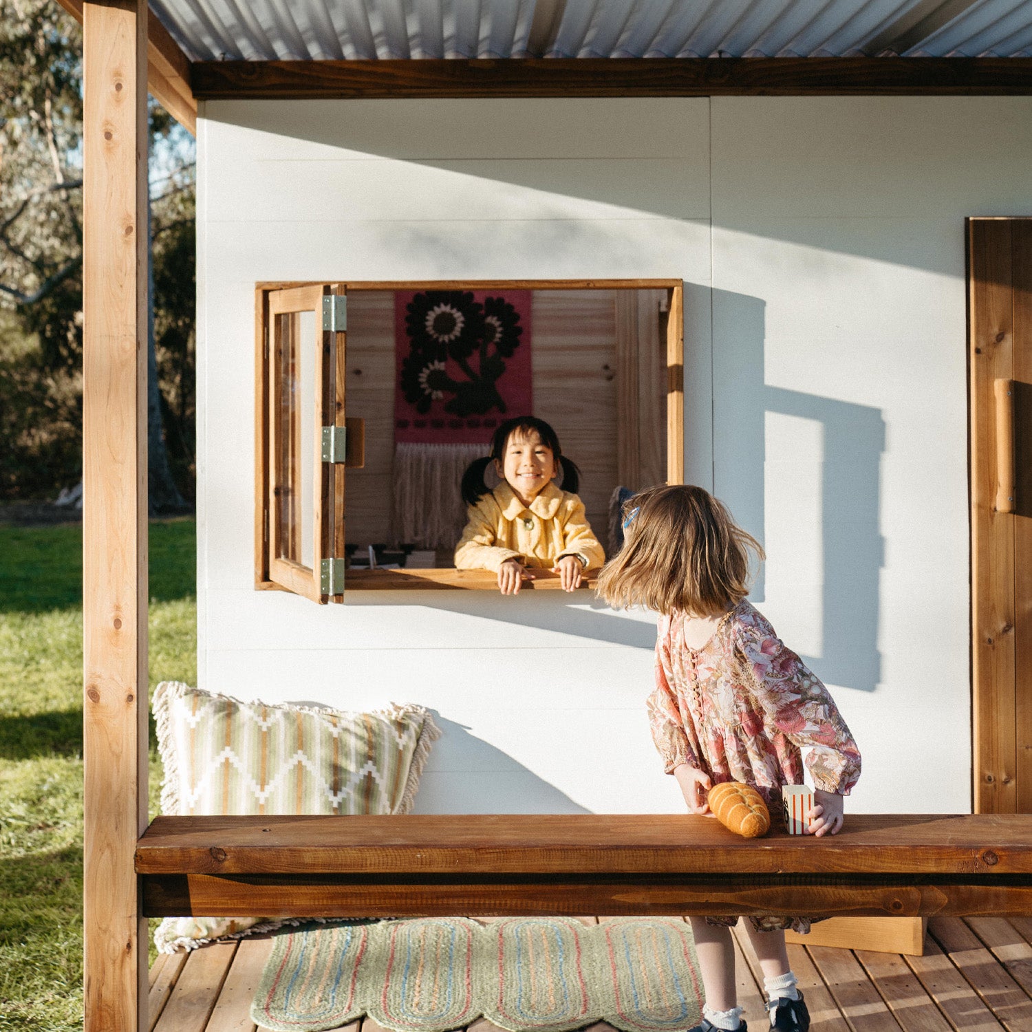 Children playing through the service window of a stylish outdoor wooden cubby