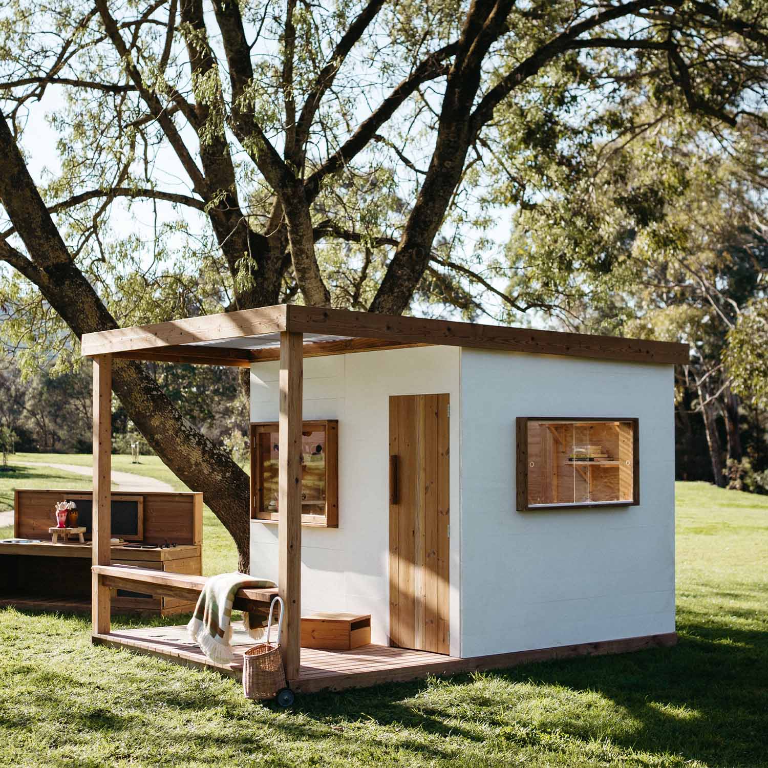 Angled view of cubby house showing timber door and double windows under corrugated roof