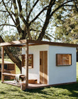 Angled view of cubby house showing timber door and double windows under corrugated roof