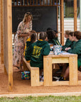 Teacher and class sitting at a timber outdoor table and bench seat in a school garden shade structure