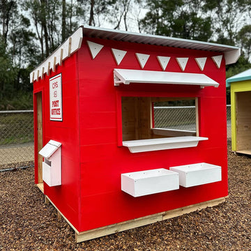 A red and white painted wooden cubby house styled as a post office in an education village play space