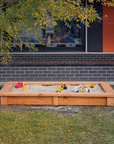 Raised timber sandpit in school grounds with toys and building in background