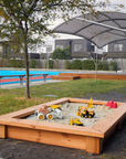 Raised timber sandpit in school grounds with toys and timber deck in background