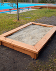 Raised timber sandpit in school grounds with blue playing fields in the background