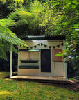 A painted timber cubby house with a verandah in a backyard garden