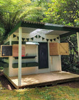 A wooden cubby house with a front porch verandah in dappled sunlight in a leafy garden