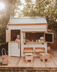 A child plays inside a beautiful white painted wooden pitched roof cubby house with accessories and toys