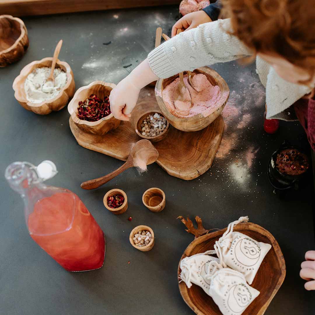 A child mixing potions and nature items like flower buds with water and making fizzy concoctions - they are having a sensory play session on a sensory play table.