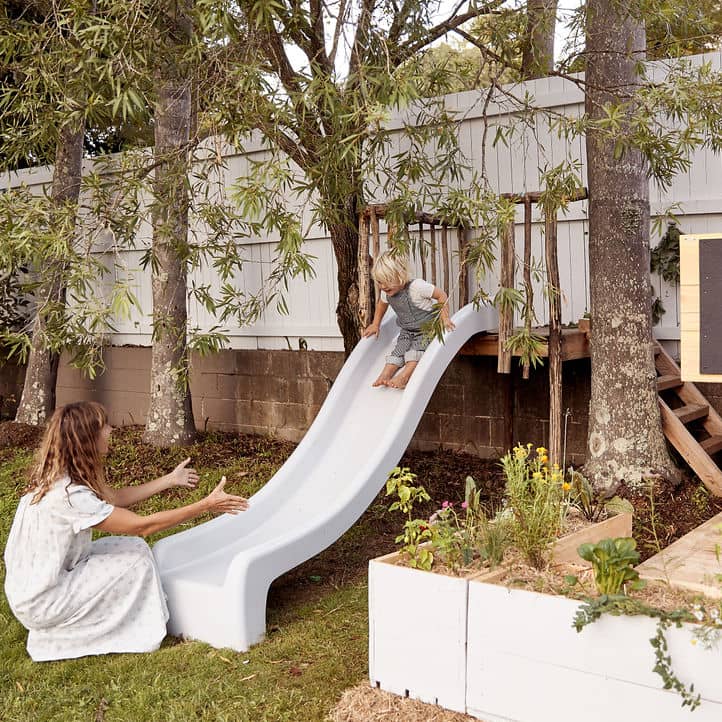 A woman waits to catch her child at the end of a white slide