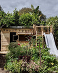 A cubby and wooden platform with slide are nestled into a beautiful overgrown garden