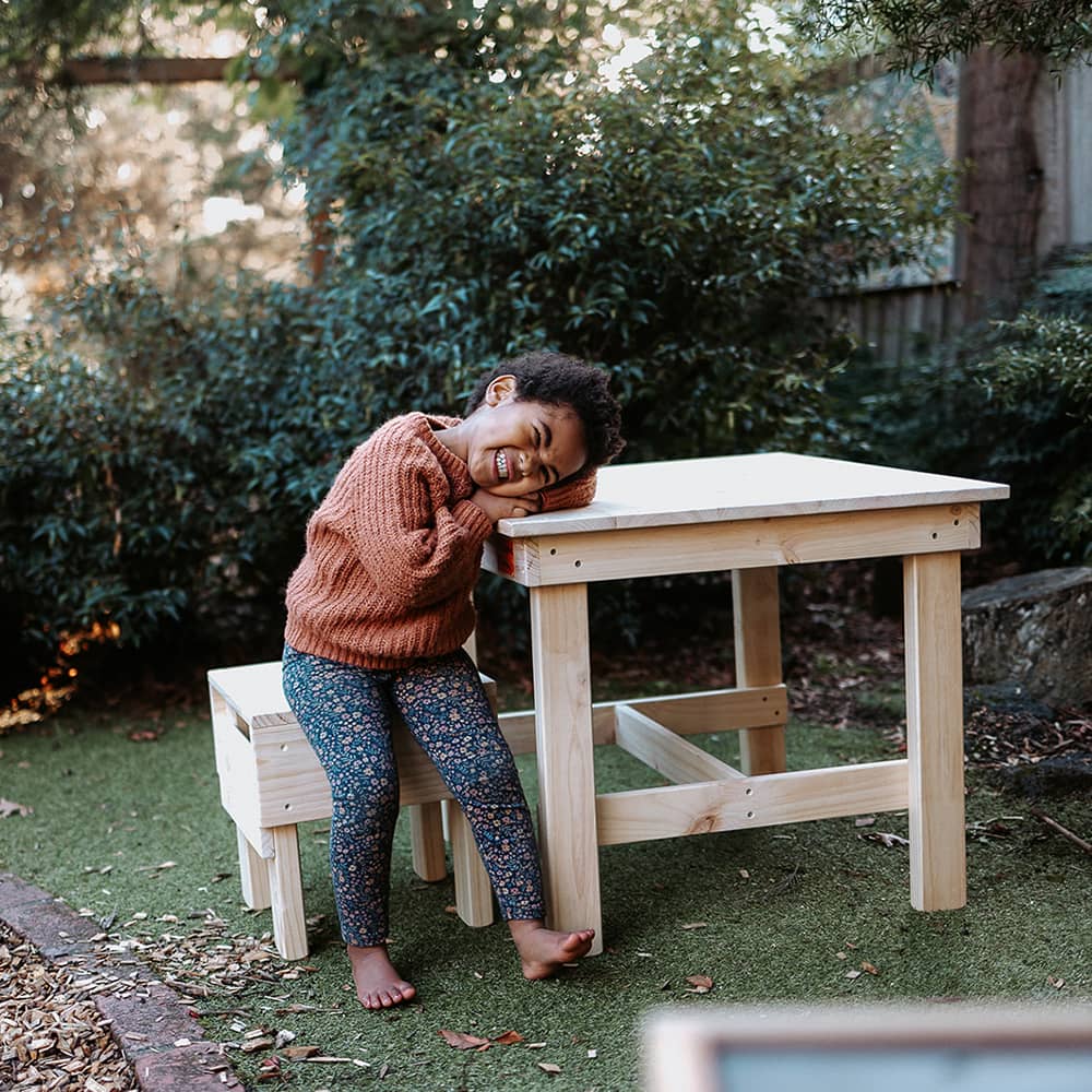 A smiling girl sitting at a pine wooden kids table