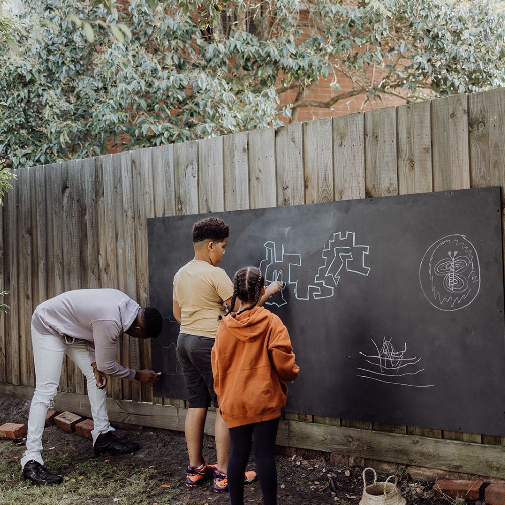 A family enjoying and drawing on their outdoor fence blackboard