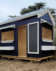 A painted wooden cubby house with a pitched roof and accessories in an education setting