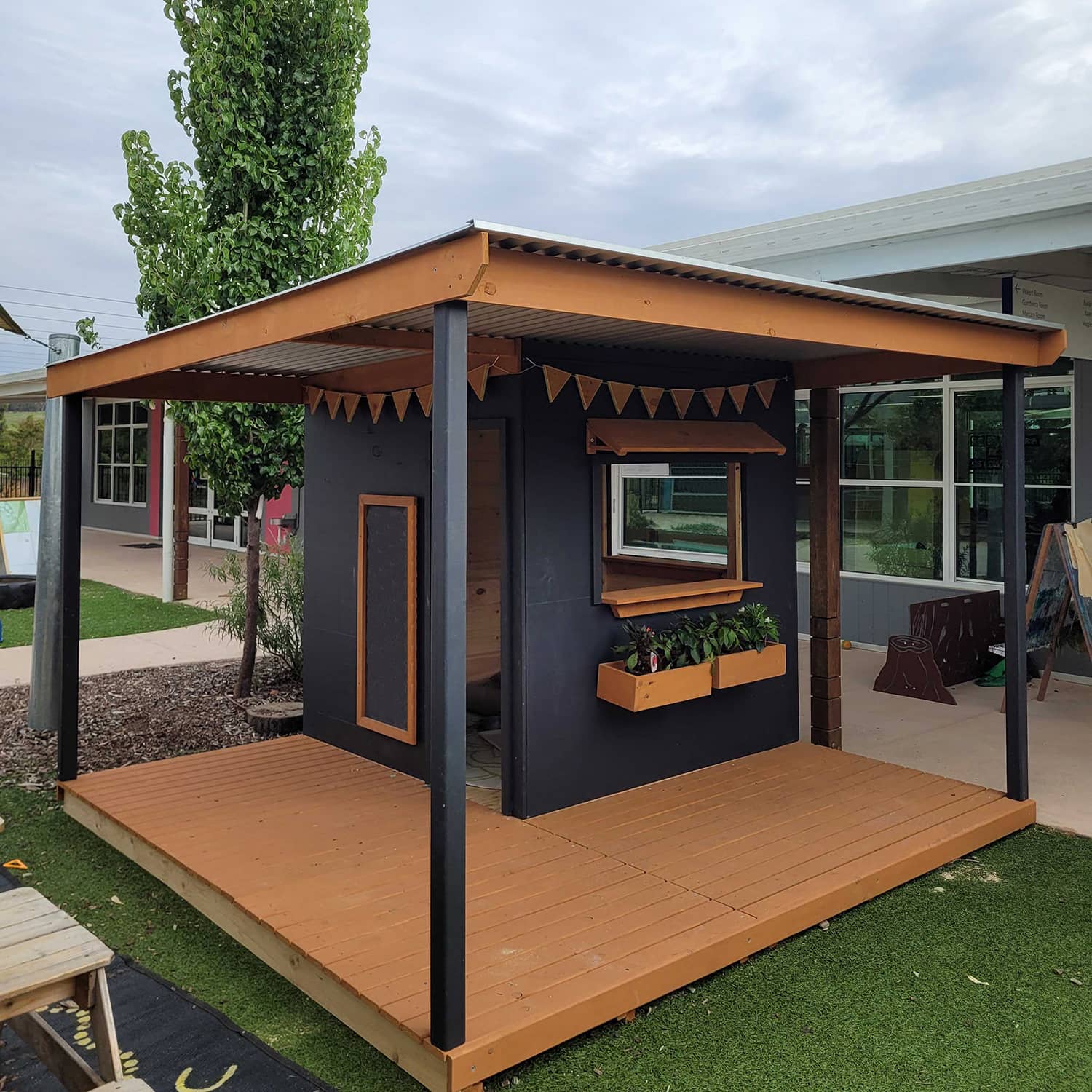 A painted wooden cubby house with a wraparound verandah and deck in an education setting