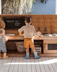 A baby and preschooler play at a wooden play kitchen with oven