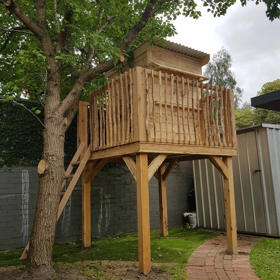 A raised platform with cubby house next to a tree in a family backyard